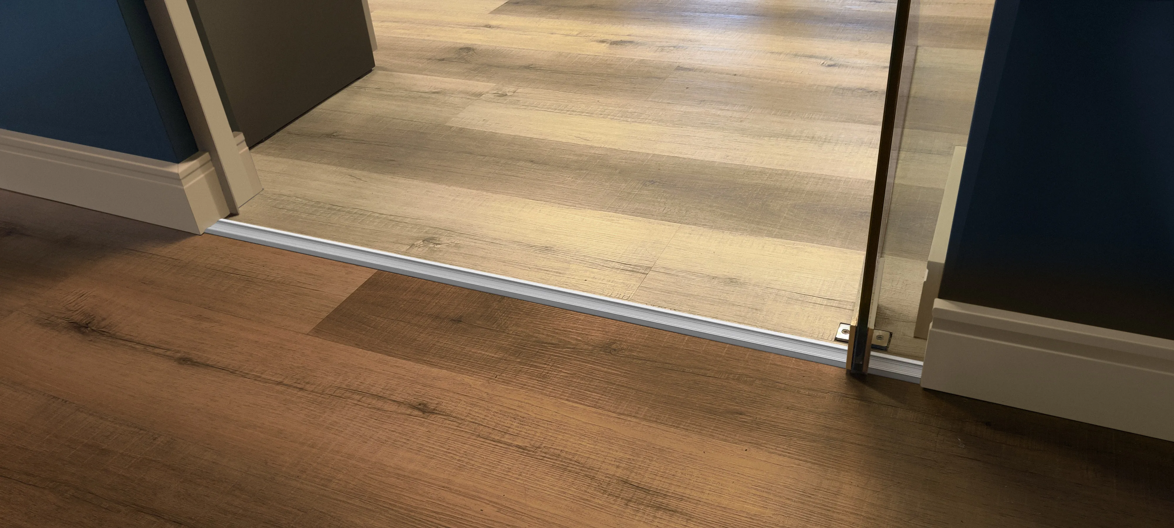 Perfil para pisos flotantes y alfombras Atrim colocado entre dos pisos de madera, ideal para cubrir juntas y resolver transiciones entre ambientes